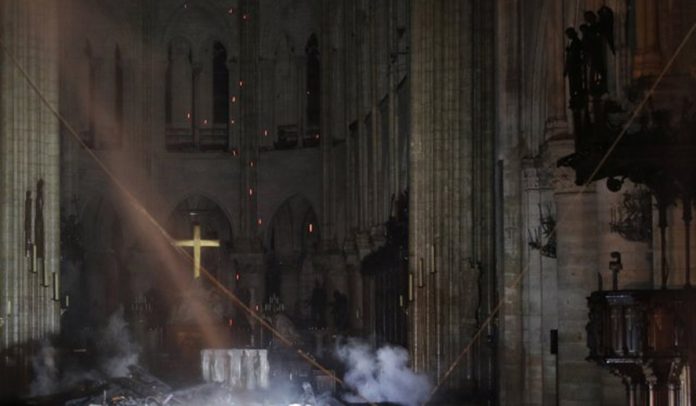 Smoke rises around the alter in front of the cross inside the Notre Dame Cathedral as a fire continues to burn in Paris