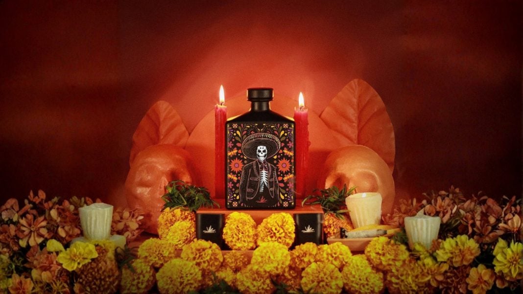 Botella de tequila personalizada junto a fotografías, cempasúchil y veladoras en una ofrenda de Día de Muertos.